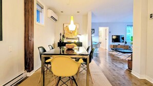 A dining area with a glass table, chairs, and a chandelier. There is a television in the background. - Luxury Duplex in a Prime Location (Gatineau)