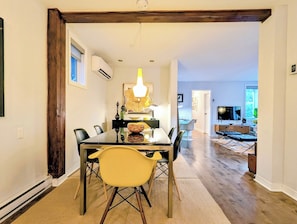 A dining area with a glass table, chairs, and a chandelier. There is a television in the background. - Luxury Duplex in a Prime Location (Gatineau)