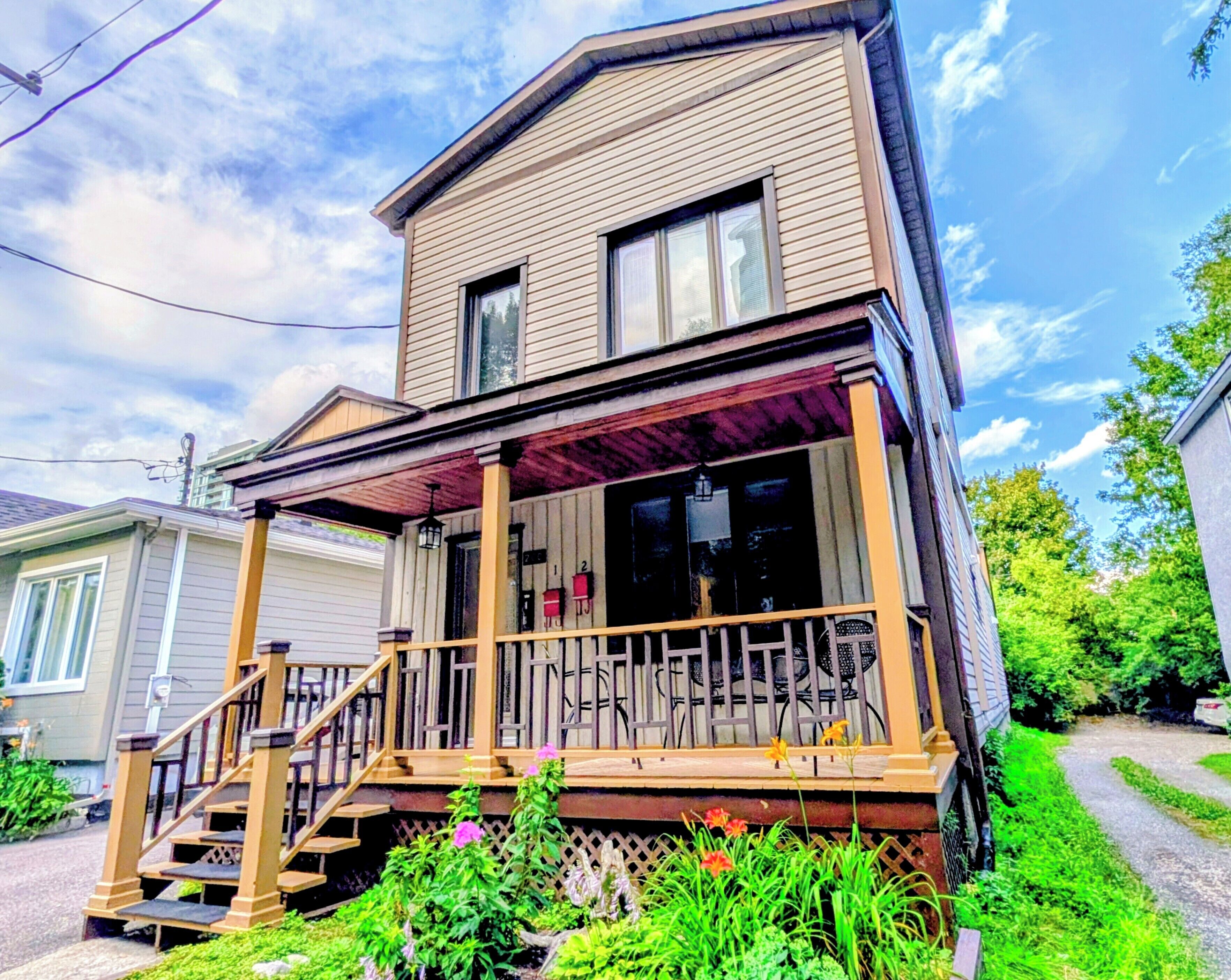 A two-story house with a front porch, a staircase leading to the entrance, and a small garden area with flowers.