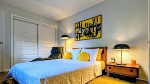 A bedroom with a bed, two bedside lamps, a nightstand, a clock, and a painting on the wall. - Luxury Duplex in a Prime Location (Gatineau)