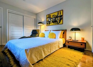 A bedroom with a bed, two bedside lamps, a nightstand, a clock, and a painting on the wall. - Luxury Duplex in a Prime Location (Gatineau)