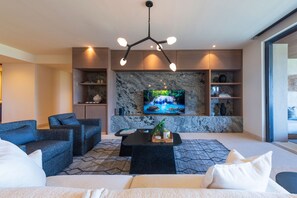 A modern living room with a large flat-screen TV mounted on a marble wall, a black coffee table, and a sofa with white cushions. - Condo Sardan 3BD - Tau Punta Mita (Punta de Mita)