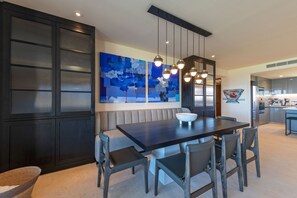 A modern dining area with a dark wooden table, grey upholstered bench, and contemporary pendant lighting. - Condo Sardan 3BD - Tau Punta Mita (Punta de Mita)