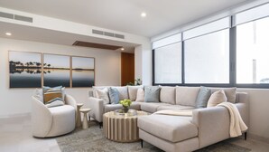 Een moderne woonkamer met een hoekbank, een ronde salontafel en een groot raam dat voor natuurlijk licht zorgt.