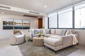 A modern living room with a sectional sofa, a round coffee table, and a large window providing natural light. - Amor y Surf 5BD - Surf Punta Mita (Punta de Mita)