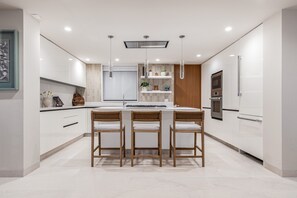 A modern kitchen with a central island, white cabinetry, and a wooden dining set. - Amor y Surf 5BD - Surf Punta Mita (Punta de Mita)