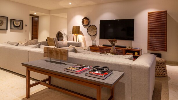 Una sala de estar moderna con un sofá grande en forma de L, una mesa de centro, un televisor de pantalla plana y decoración en la pared.