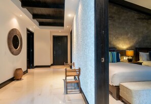 A modern hotel room with a large bed, a wooden chair, a round mirror, and a textured wall. - Condo Jazmin 4BD - Hacienda De Mita Punta Mita (Punta de Mita)