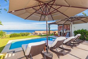 Ein Poolbereich mit Liegestühlen und Sonnenschirm, mit Blick auf das klare, blaue Meer.