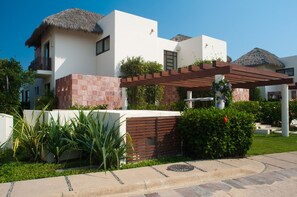Ein modernes Gebäude mit weißer Fassade, einem Reetdach und einer Holzpergola.