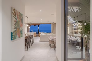 A modern interior with a dining area, a sofa, and a view of the ocean. - Condo Joya 3BD - Marietas Punta Mita (Punta de Mita)