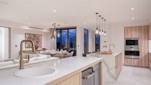 Una cucina moderna con un'isola grande, elettrodomestici integrati e illuminazione a sospensione.