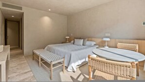 Ein Schlafzimmer mit einem Bett, Nachttischen, einer Bank, einem runden Tisch und Korbstühlen.