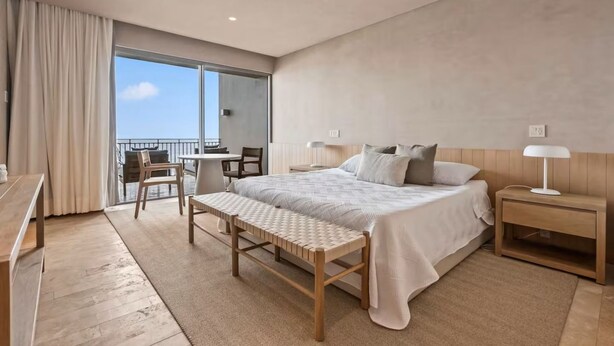 Ein modernes Hotelzimmer mit einem großen Bett, einer Holzbank, einem Schreibtisch und einem Balkon mit Blick.