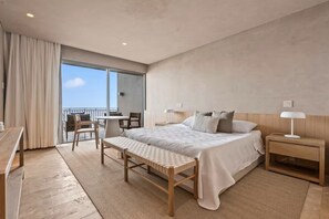 A modern hotel room with a large bed, a wooden bench, a desk, and a balcony with a view. - Condo Perla de Mar 4BD - Uavi (Punta de Mita)