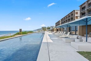 A poolside area with lounge chairs and a view of the ocean. - Condo Perla de Mar 4BD - Uavi (Punta de Mita)