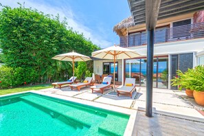 A pool area with lounge chairs and umbrellas, a clear view of the ocean, and a modern building with large windows. - Villa Perla 3BD - Porta Fortuna Punta Mita (Punta de Mita)