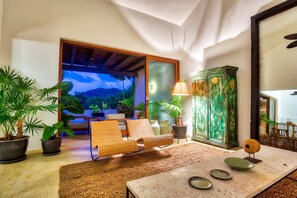 A room with a large sliding glass door leading to a balcony, wicker furniture, a cabinet, and a table with decorative plates. - Condo Pac Fico 3BD - Terrazas Punta Mita (Punta de Mita)