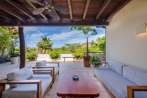 An outdoor patio with a wooden ceiling, a ceiling fan, and a view of a lush garden with trees and a hill in the distance. - Condo Pac Fico 3BD - Terrazas Punta Mita (Punta de Mita)
