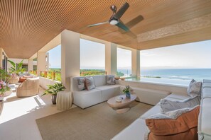A spacious living area with a large window overlooking the ocean, a ceiling fan, and a seating arrangement. - Condo Surf 4BD - Surf Punta Mita (Punta de Mita)