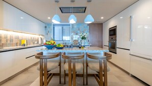 A modern kitchen with a central island, wooden stools, a fruit bowl, and a view of the city. - Condo Surf 4BD - Surf Punta Mita (Punta de Mita)
