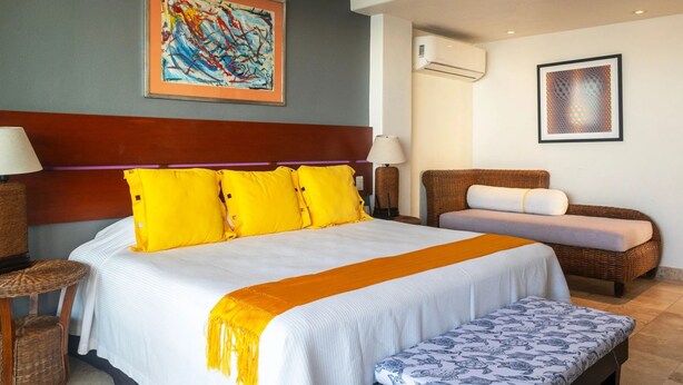 Habitación de hotel con una cama grande, un sofá, un banco y dos cuadros en las paredes.