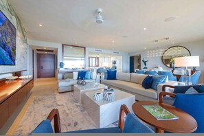 A modern living room with a sofa, coffee table, and chairs. There is a dining area with a table and chairs. The room has a large mirror and a ceiling light. - Casa Escrita 3BD - Tau Punta Mita (Punta de Mita)
