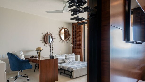 A modern bedroom with a desk, a blue chair, a bed with striped bedding, and two wall-mounted mirrors. - Casa Escrita 3BD - Tau Punta Mita (Punta de Mita)
