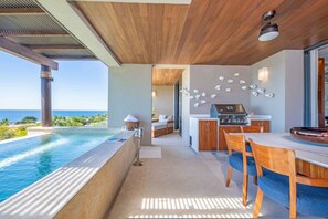 Eine moderne Außenküche mit Pool und Essbereich, mit Blick auf eine schöne Aussicht.