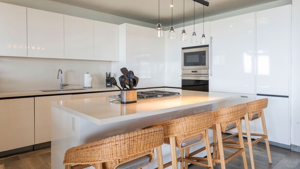 A modern kitchen with white cabinetry, a central island with bar stools, a stainless steel range hood, and pendant lighting. - Ph Bugambilia 4BD - Tau Punta Mita (Punta de Mita)