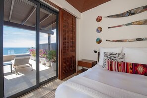Ein Schlafzimmer mit einem großen Bett, einer Holztür, einem kleinen Nachttisch und Meerblick durch eine Schiebetür.
