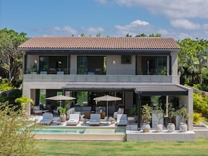 Ein modernes, zweistöckiges Haus mit Swimmingpool, Sitzgelegenheiten im Freien und üppiger Bepflanzung.