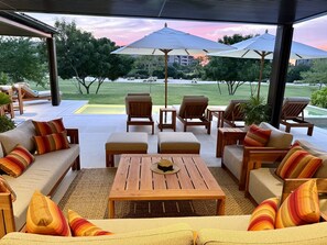 An outdoor seating area with wooden furniture and striped cushions, overlooking a well-maintained lawn and trees. - Villa Amada 5BD - Porta Fortuna Punta Mita (Punta de Mita)