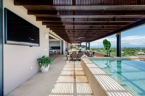 Ein überdachter Außenbereich mit Pool, Essbereich und Blick auf die Landschaft.