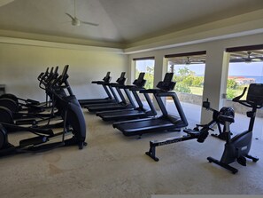Ein Fitnessstudio mit Laufbändern, Crosstrainern und einem stationären Fahrrad, mit großen Fenstern und Blick ins Freie.