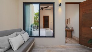 A modern interior with a grey sofa, a large sliding glass door, and a wooden door leading to a bathroom. - Casa Tuki 6BD - Las Vistas Punta Mita (Punta de Mita)