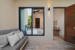 A modern interior with a grey sofa, a large sliding glass door, and a wooden door leading to a bathroom. - Casa Tuki 6BD - Las Vistas Punta Mita (Punta de Mita)