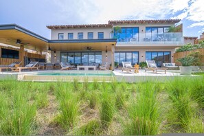 Ein modernes, zweistöckiges Haus mit Swimmingpool, Sitzgelegenheiten im Freien und einer überdachten Terrasse.