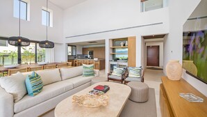 A modern living room with a sofa, coffee table, and a dining area with a kitchen in the background. - Villa Cielo Azul 4BD - Iyari Punta Mita (Punta de Mita)