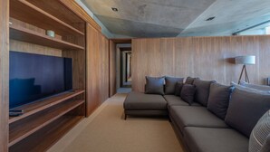 A modern living room with a sectional sofa, a flat-screen TV on a wooden stand, and a lamp. - Casa Morgandez 5BD - Iyari Punta Mita (Punta de Mita)