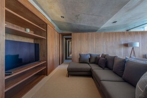 Ein modernes Wohnzimmer mit einem Ecksofa, einem Flachbildfernseher auf einem Holzboden und einer Lampe.