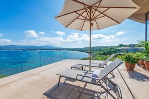 A balcony with a view of a beach and ocean, lounge chairs, and a large umbrella. - Casa Morgandez 5BD - Iyari Punta Mita (Punta de Mita)