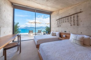 A hotel room with two beds, a desk, and a view of the sea.