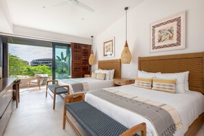 A modern hotel room with a large bed, two bedside tables, a desk, and a chair. There are two windows with a view of greenery and buildings outside. - Villa Amistad 4BD - Porta Fortuna Punta Mita (Punta de Mita)