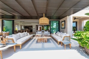 An outdoor living area with a modern design, featuring a large sofa set, a coffee table, and a hanging light fixture. - Villa Amistad 4BD - Porta Fortuna Punta Mita (Punta de Mita)