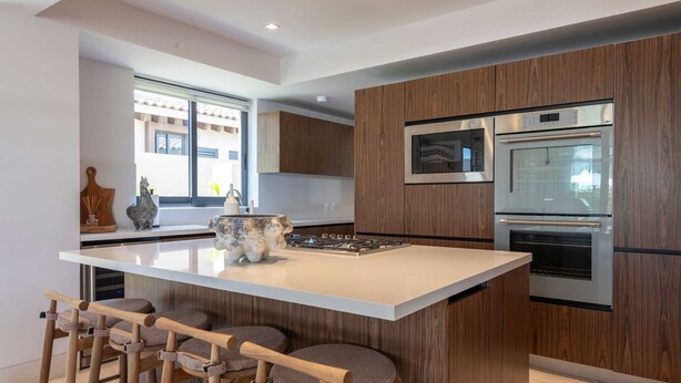 Una cocina moderna con una isla central, taburetes de bar, microondas y hornos empotrados.