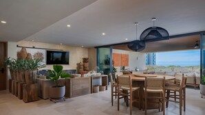 Un salón amplio con una gran mesa de comedor, múltiples sillas y plantas en macetas.