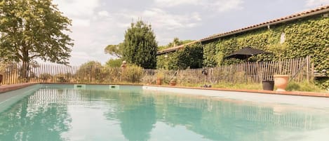 Una piscina con borde de baldosas, rodeada por una valla de madera y un edificio con tejado de cerámica.