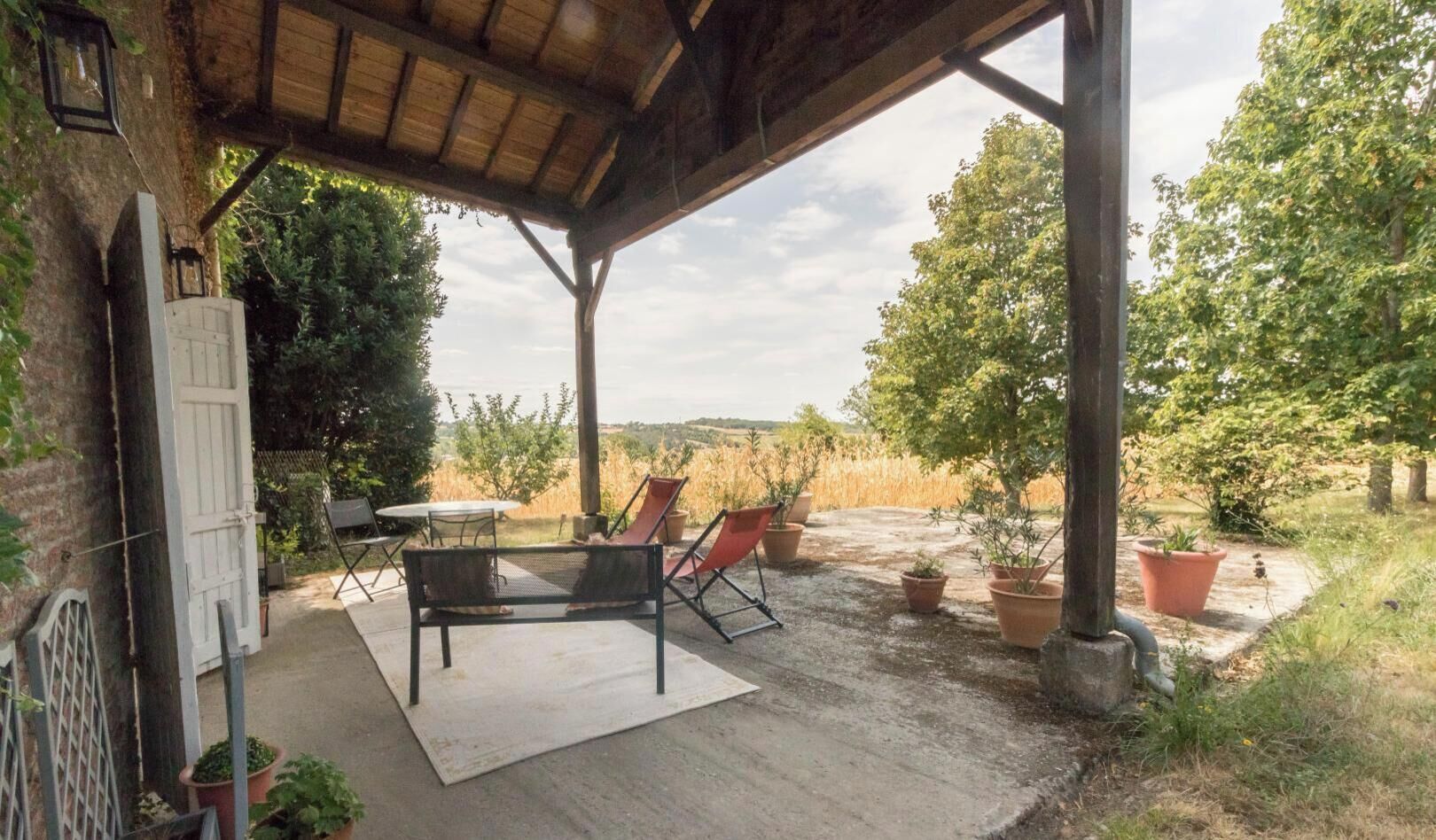 An outdoor patio with a table and chairs, surrounded by potted plants and trees.
