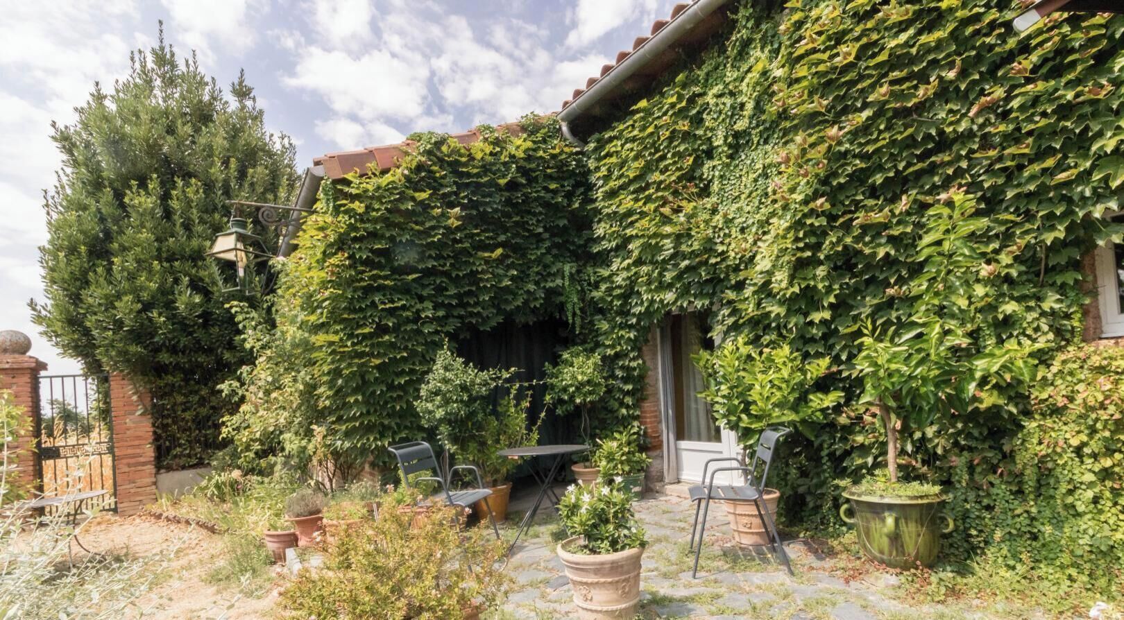 A garden with a brick wall covered in ivy, a metal gate, and outdoor seating.